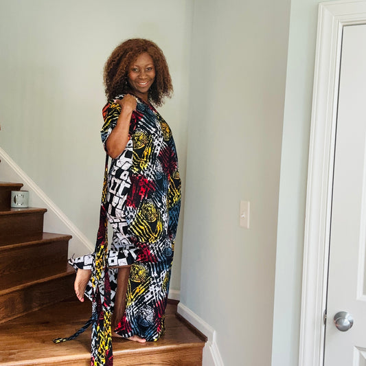 A woman standing on a staircase wearing a multicolored Ankara fringe dress with geometric patterns and tassel details.