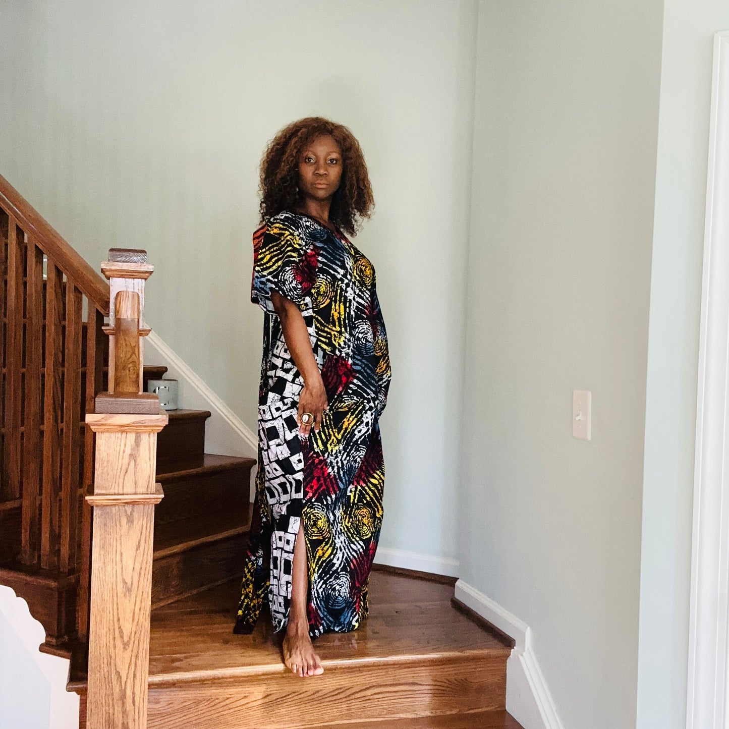 A woman standing on a staircase wearing a multicolored Ankara fringe dress with geometric patterns and tassel details.